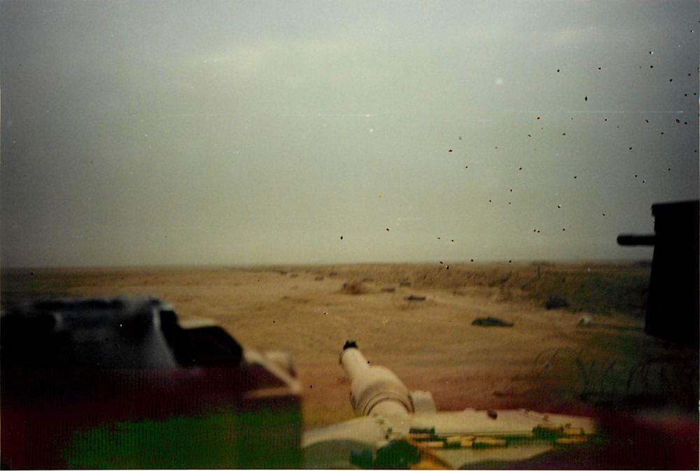 Looking out across the desert past the main gun of a tank