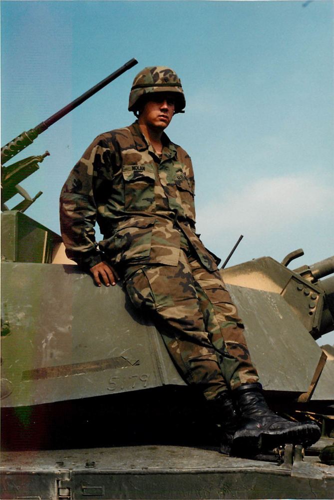 Sitting on the turret of an M1 Abrams tank, NOLAN nametape visible