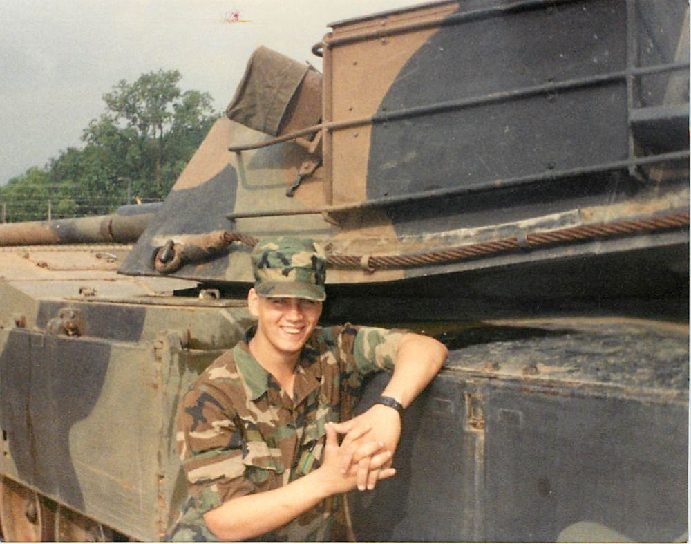 Smiling beside an M1 Abrams tank